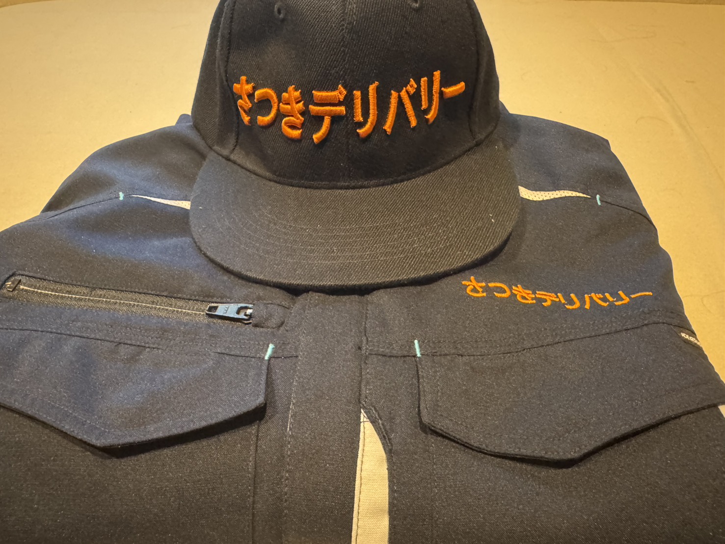 さつきデリバリーのロゴを刺繍したキャップと作業着